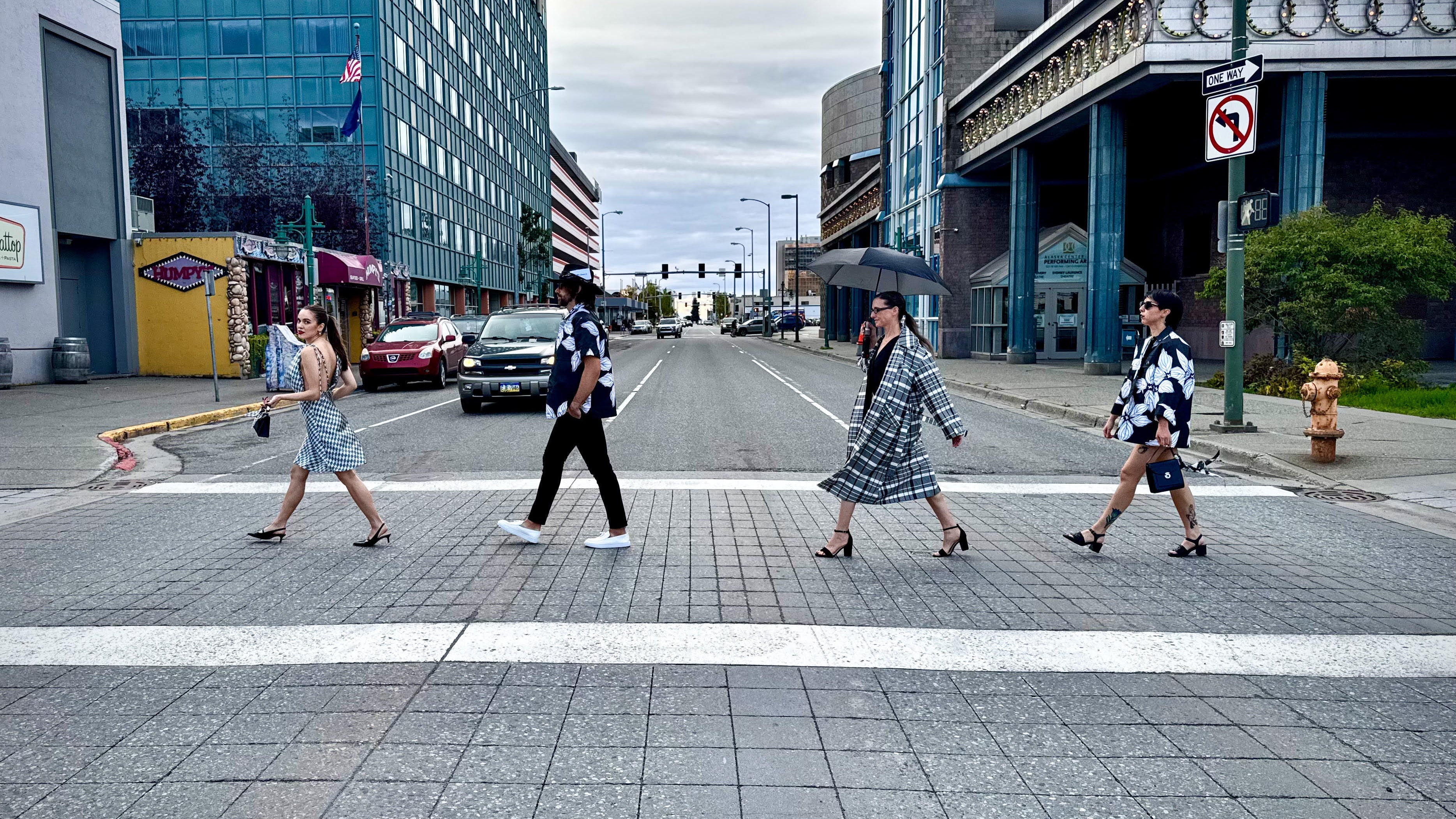 People crossing a city street with modern buildings and a fire hydrant in the background.